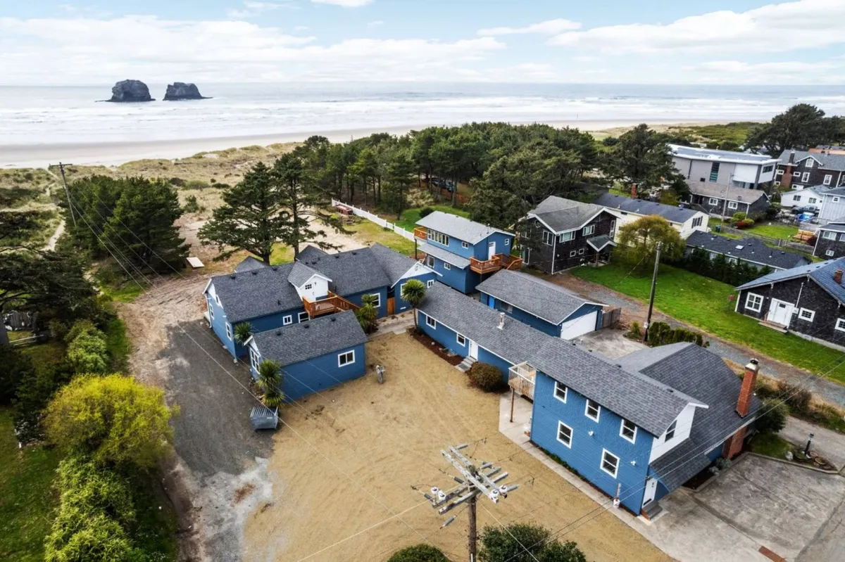A beachfront perspective looking toward the inn’s blue houses, natural greenery, and the sandy shore. This angle connects the property’s communal spaces to the nearby ocean, suggesting easy access to beach activities and panoramic views for guests.